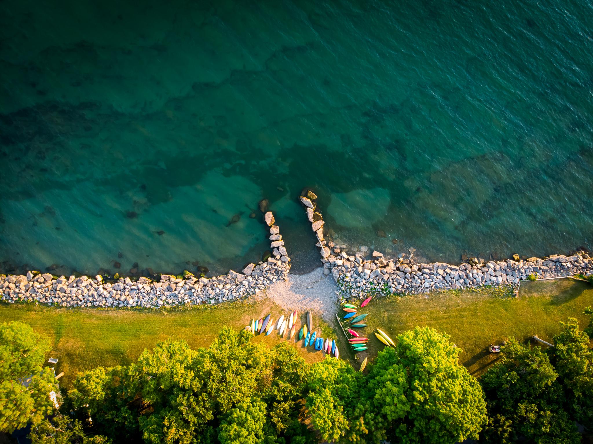 aerial image of lakeshore with rocks along shorelines, colorful canoes, and bright blue-green water